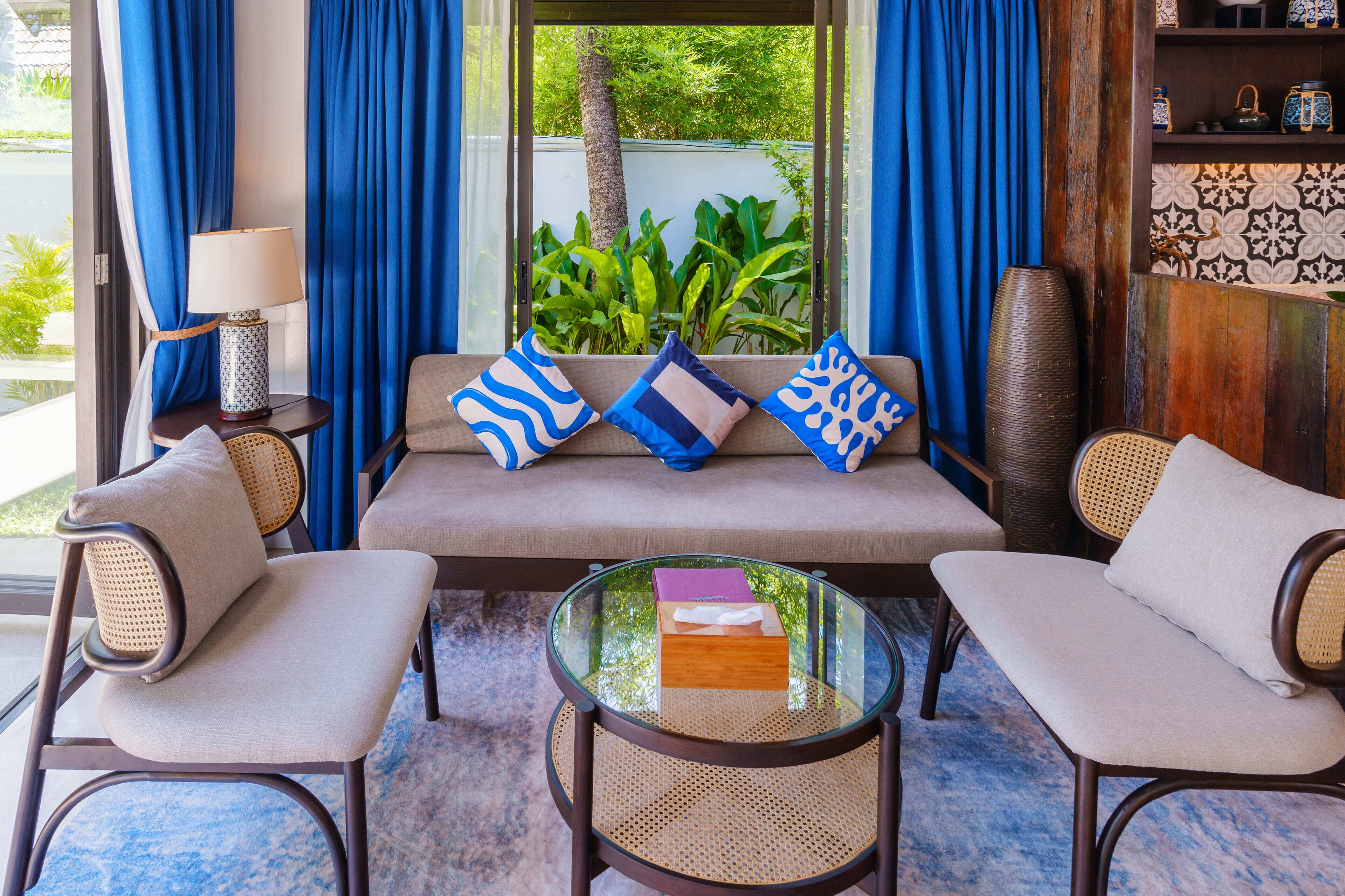 A modern living room with a sofa, two armchairs, a glass coffee table, and a side table with a lamp.