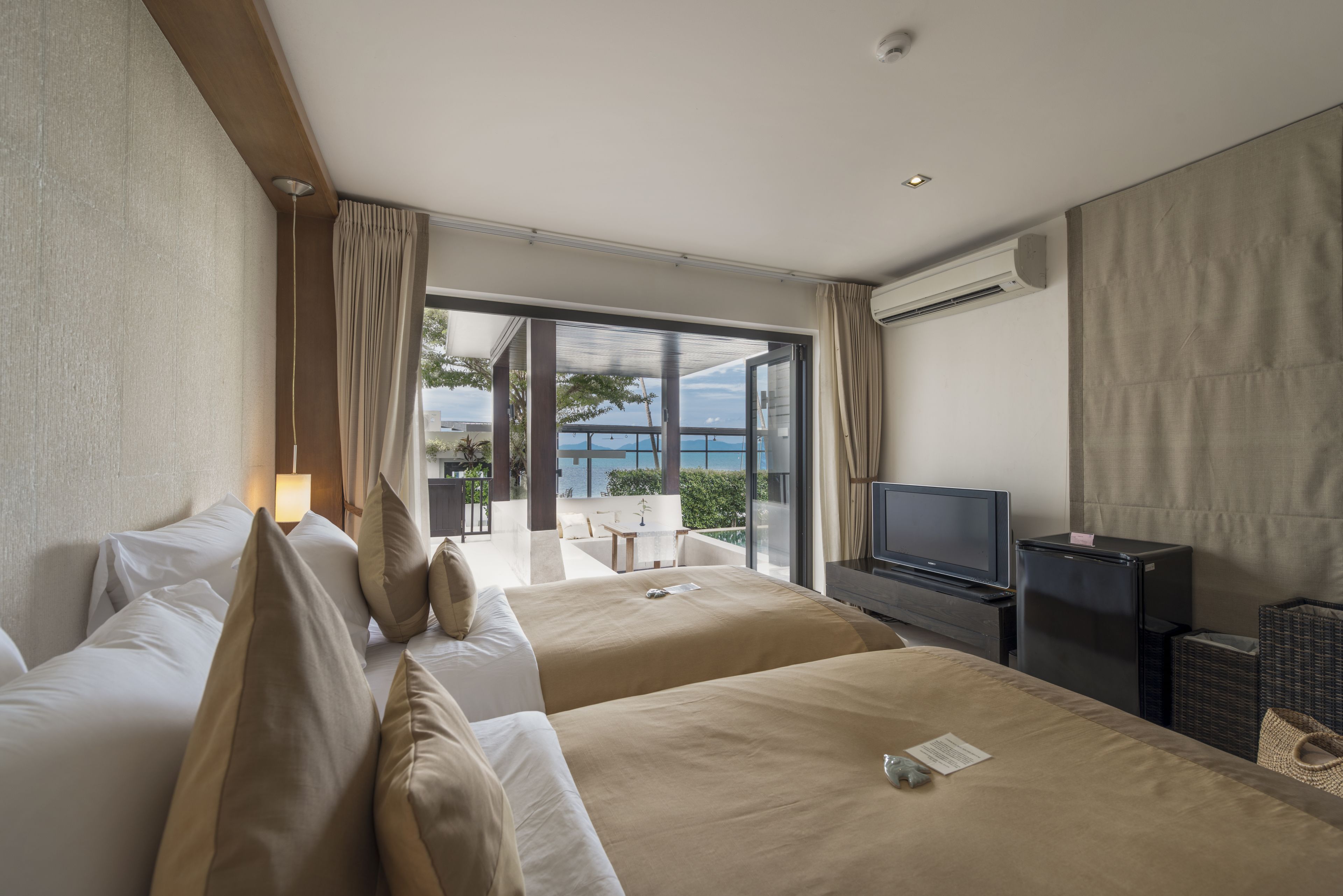 Habitación de hotel con dos camas, televisión y balcón con vista al mar.