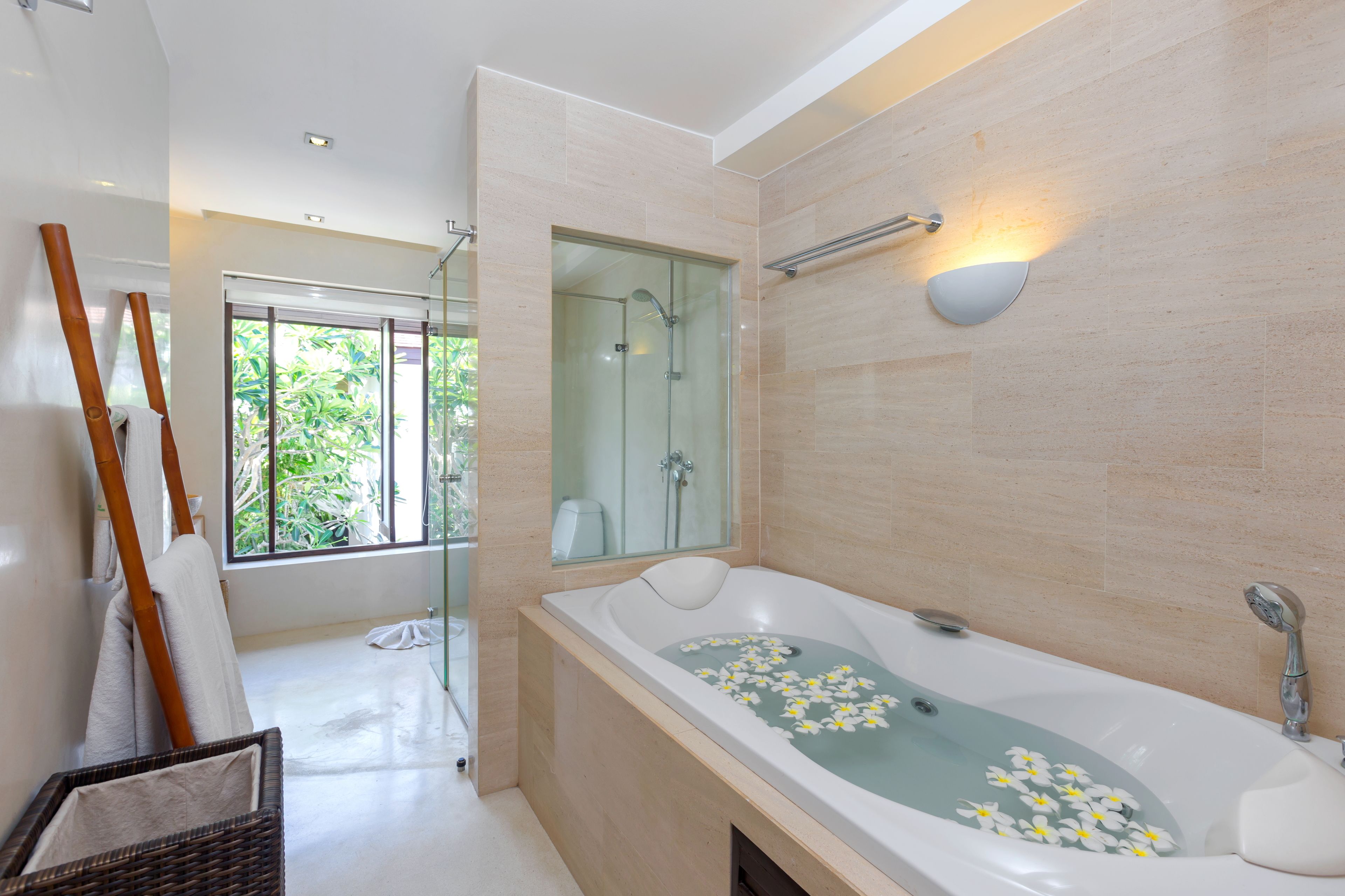 Un baño moderno con una bañera grande, un box de ducha de cristal y un ventanal con vistas a la vegetación.
