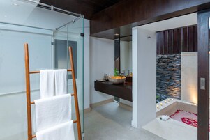 Un baño moderno con cabina de ducha de vidrio, toallero de madera, pared de acento de piedra y bañera con velas.