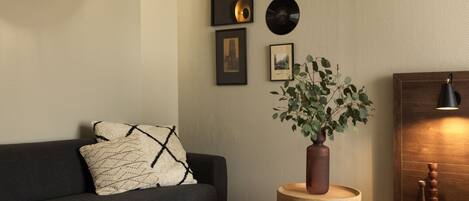 A modern living room with a dark grey sofa, a round wooden side table with a plant, and a wall decorated with framed pictures and vinyl records.