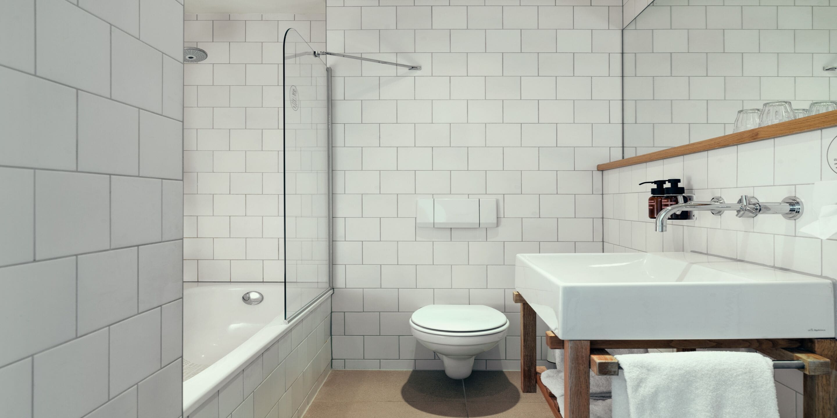 A modern bathroom with white tiles, a bathtub, a toilet, and a sink.