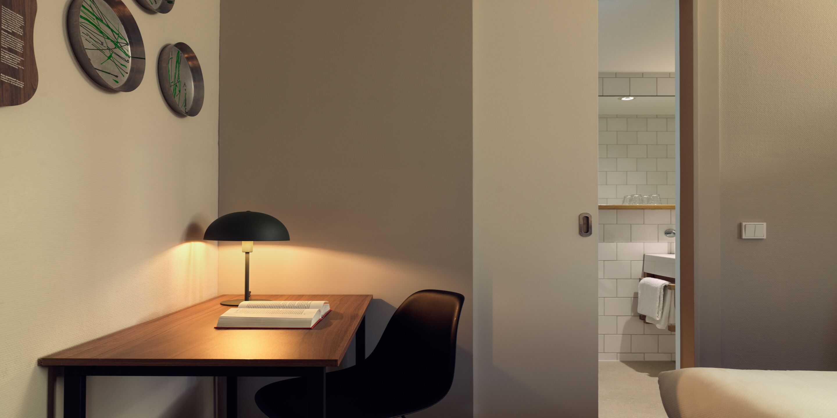 Una habitación de hotel moderna con un escritorio de madera, una silla negra, una lámpara y una cama.
