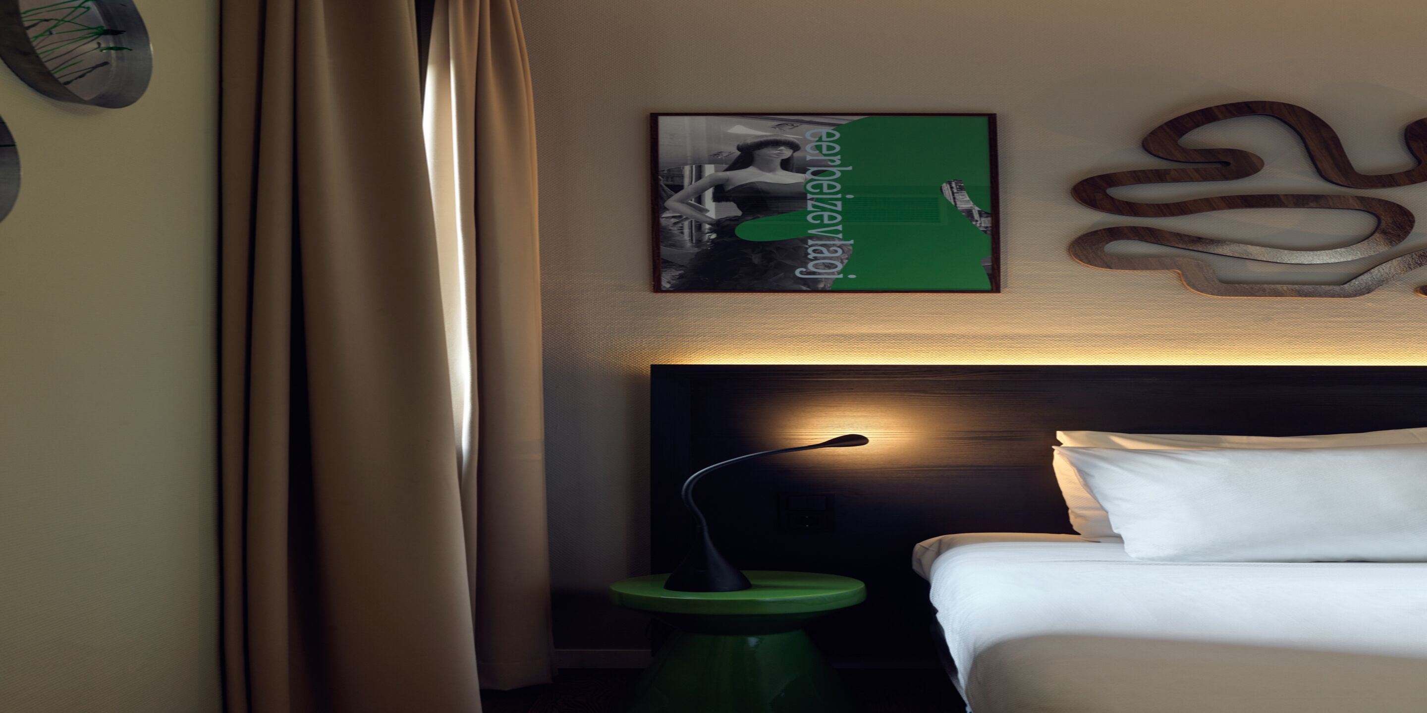 A hotel room with a bed, a nightstand, a lamp, and a wall-mounted artwork.