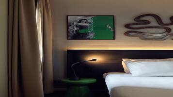 A hotel room with a bed, a nightstand, a lamp, and a wall-mounted artwork.