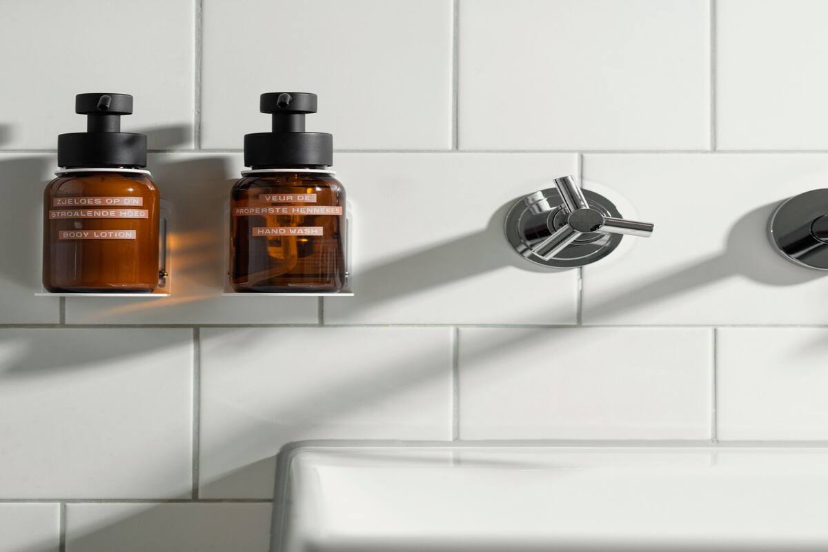 A bathroom with two bottles of body lotion and hand wash, a modern faucet, and a white tiled wall.