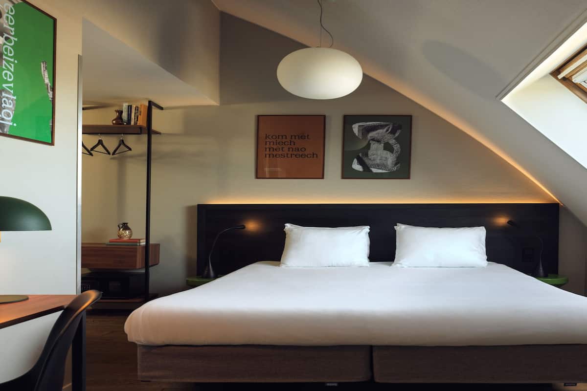 A modern bedroom with a large bed, a desk with a lamp, a hanging rack, and artwork on the walls.