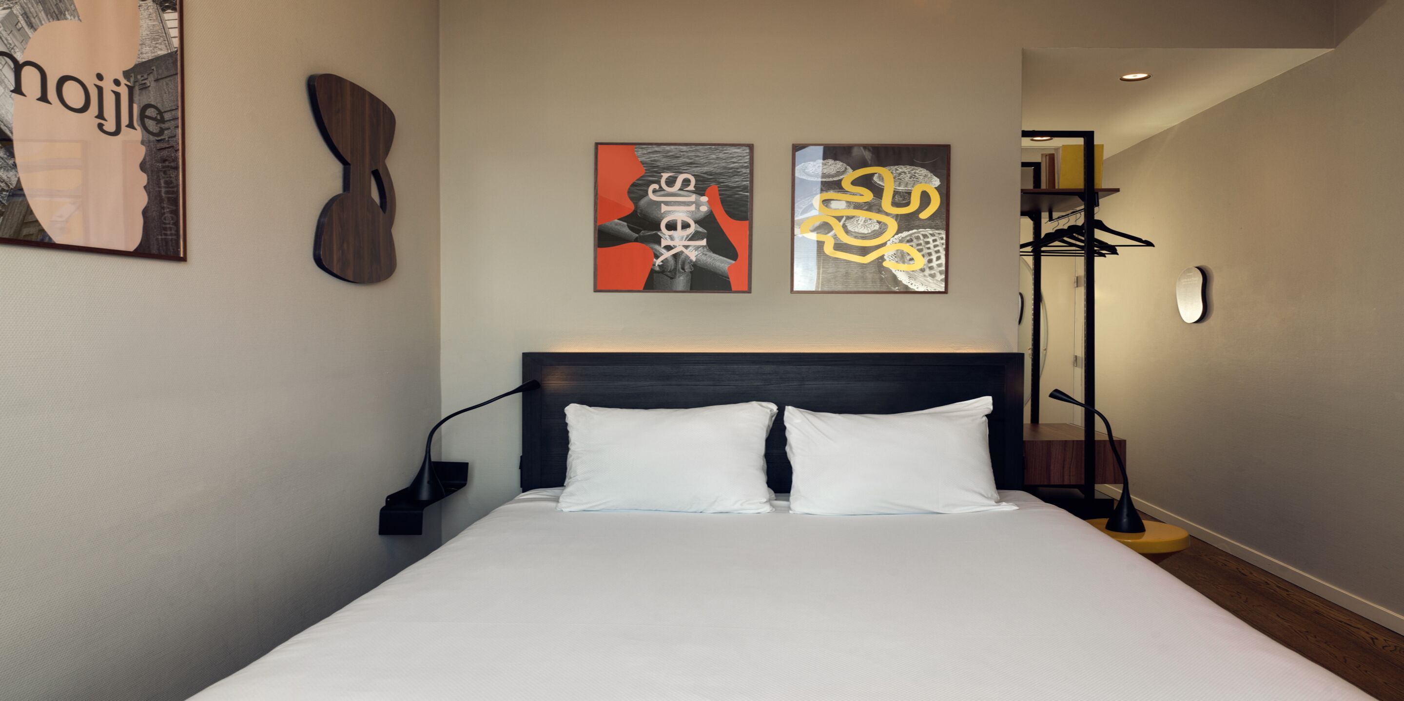 Una cama bien hecha con dos almohadas, un cabecero y dos obras de arte colgadas en la pared.