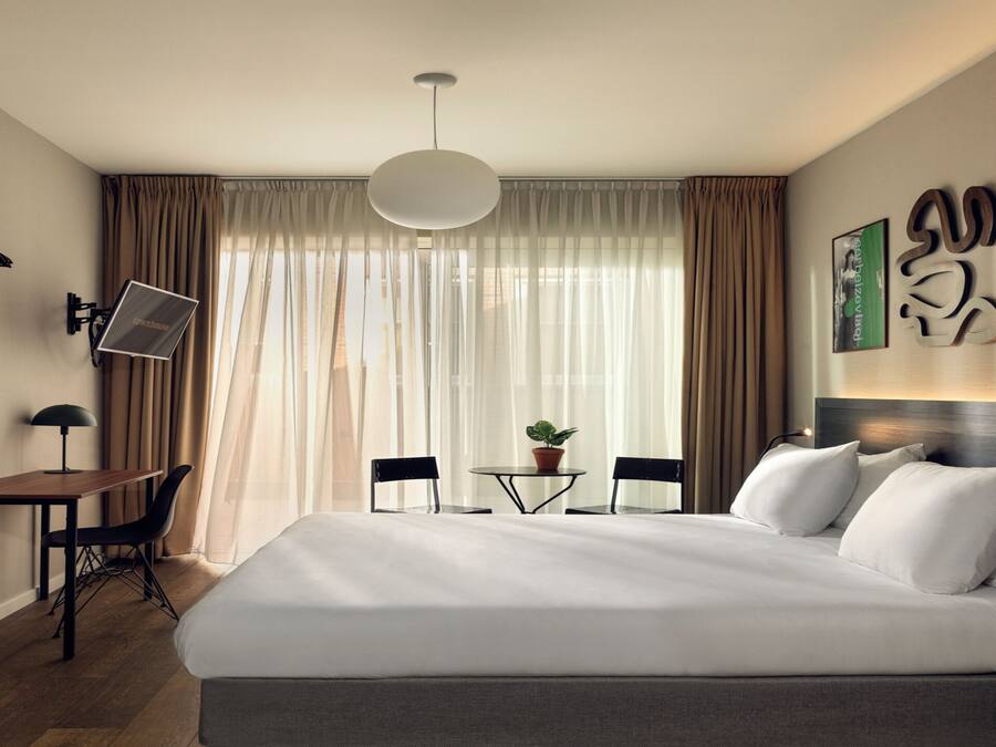 Een hotelkamer met een groot bed, een bureau met stoel, een boekenkast, een televisie en een raam met gordijnen.