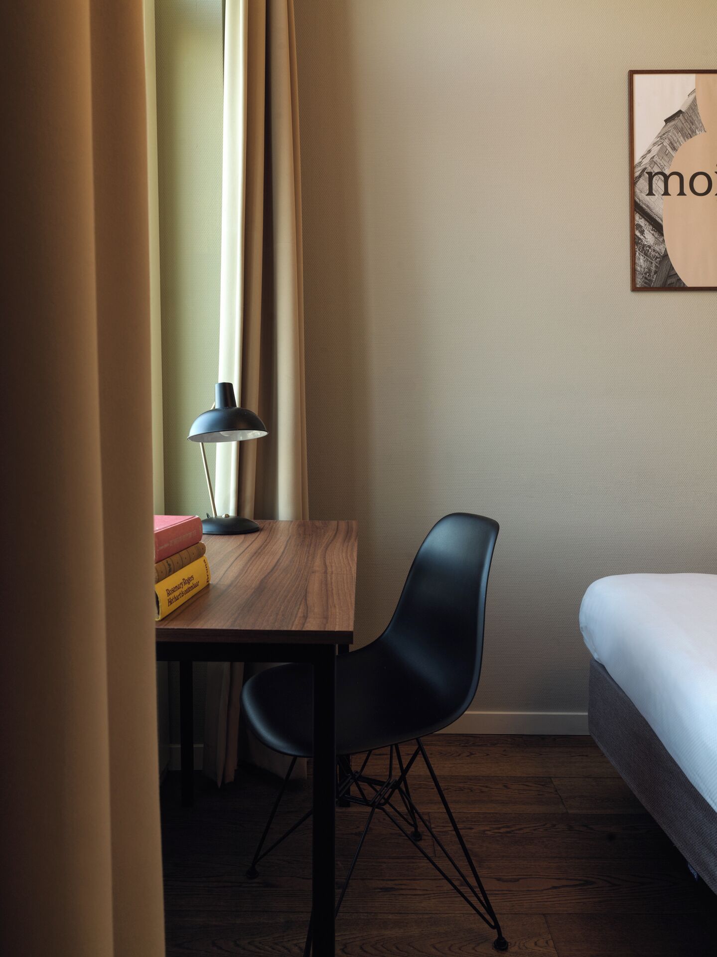 Une pièce avec un bureau en bois, une chaise noire, un lit et un tableau encadré accroché au mur.