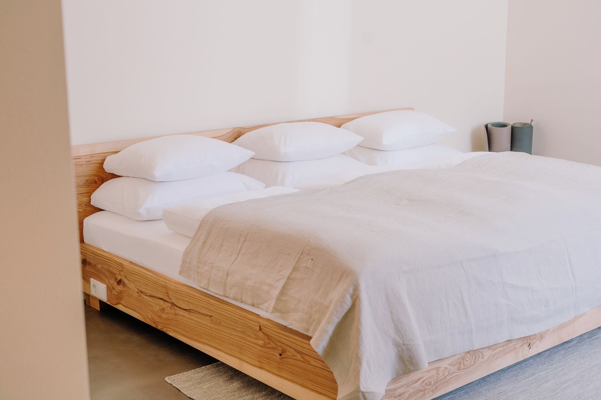 A bed with white bedding, a wooden headboard, and a grey rug.