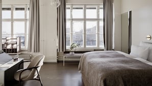 Una habitación de hotel moderna con una cama grande, un escritorio con silla, una ventana con cortinas y vistas a la ciudad.