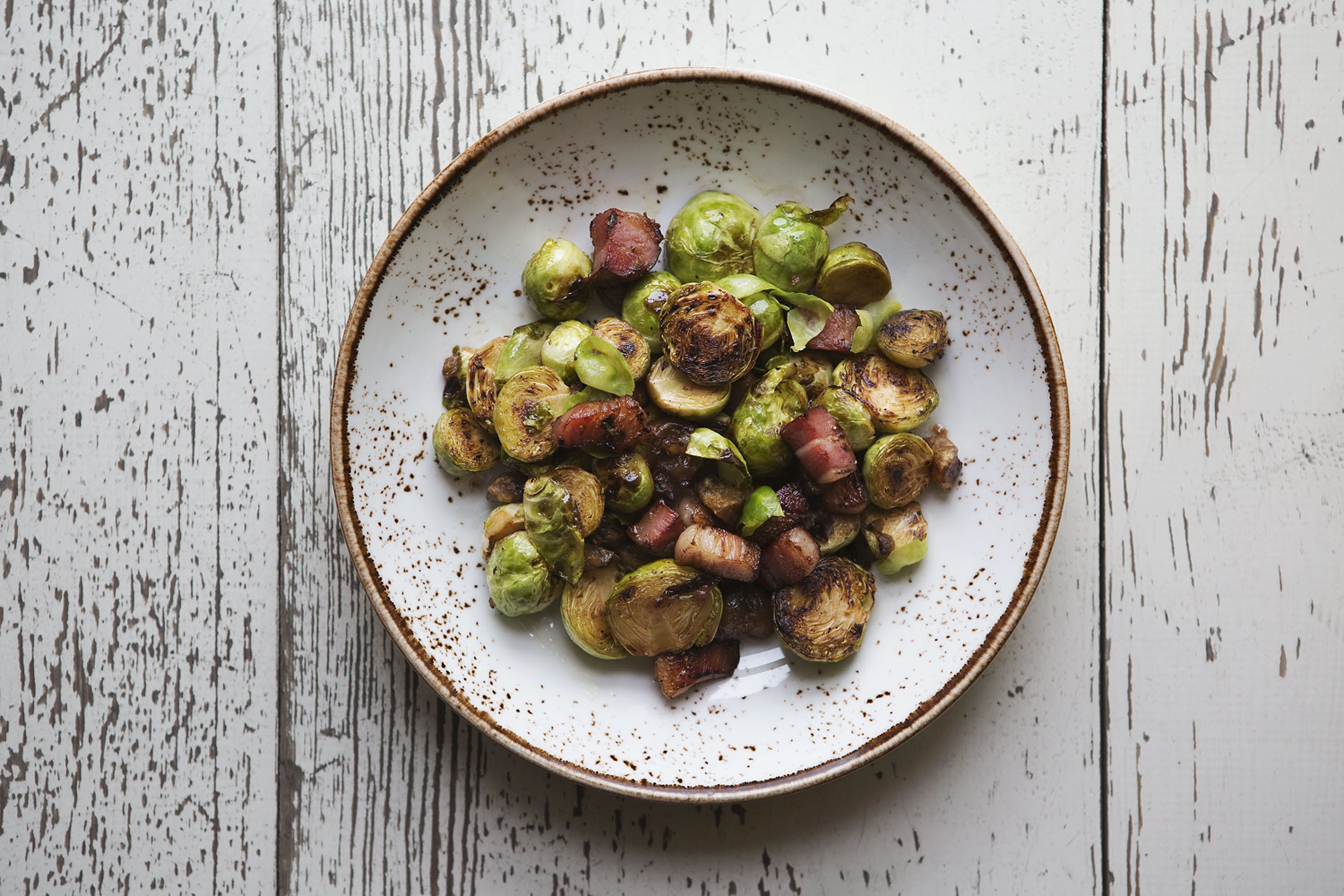 A bowl of roasted Brussels sprouts and onions on a rustic wooden table.