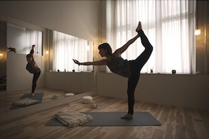 A yoga studio with a large mirror, wooden flooring, and yoga mats.