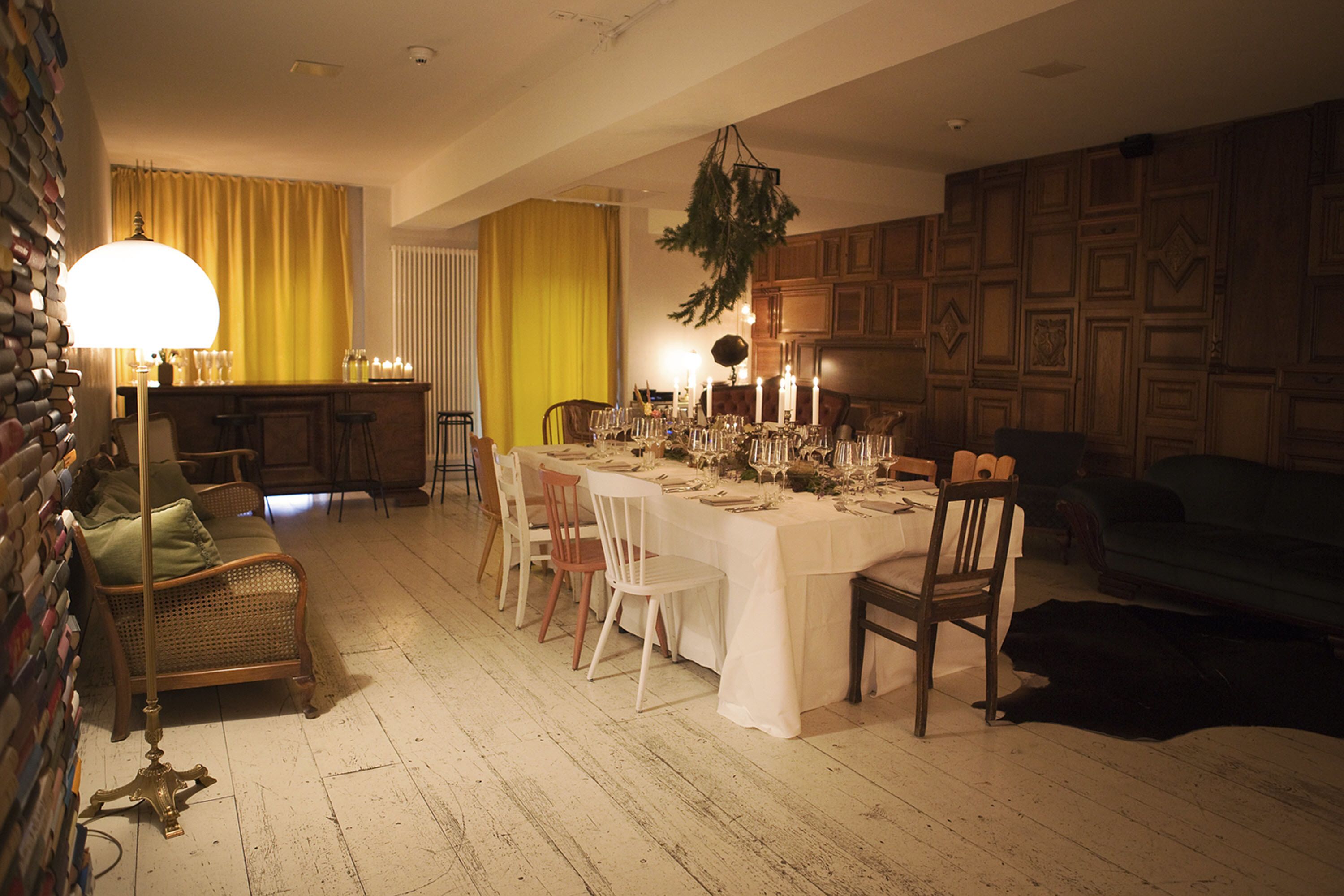 A dining area with a long table set for a meal, surrounded by chairs. A bar area with stools is visible in the background.