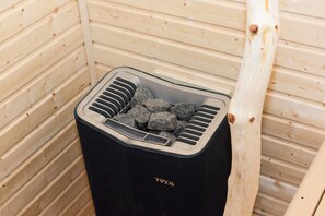 Una sauna con un recipiente negro lleno de piedras, paredes de madera y un banco de madera.