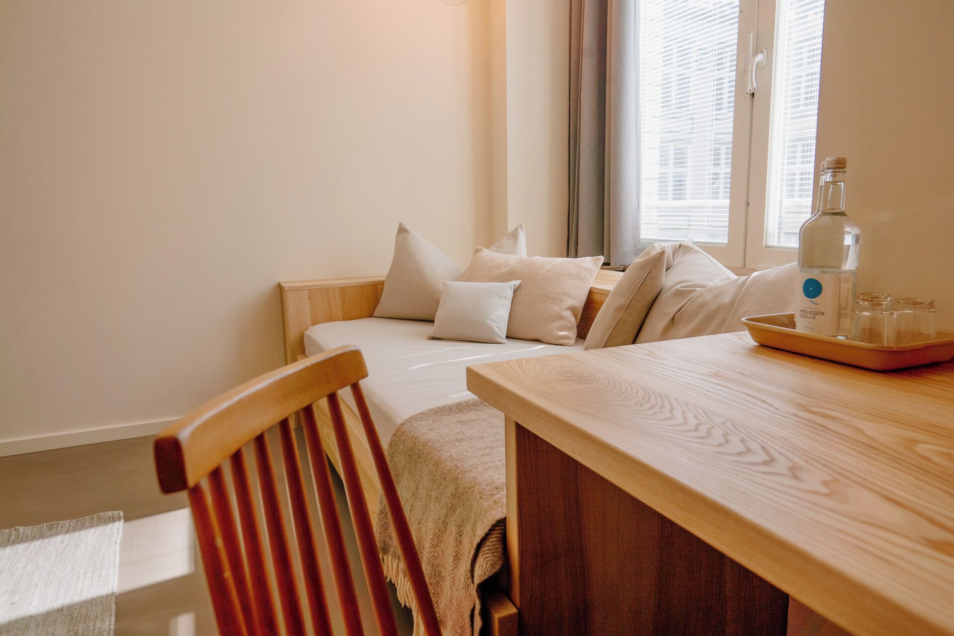 Un dormitorio con cama de madera, almohadas, una mesita de noche con una botella y vasos, y una silla.