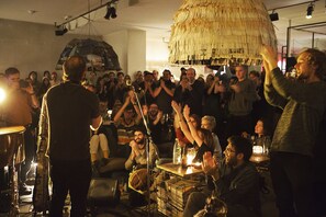 Un evento interior concurrido, con una estructura de techo de paja, un soporte para micrófono y una mesa con botellas y vasos.