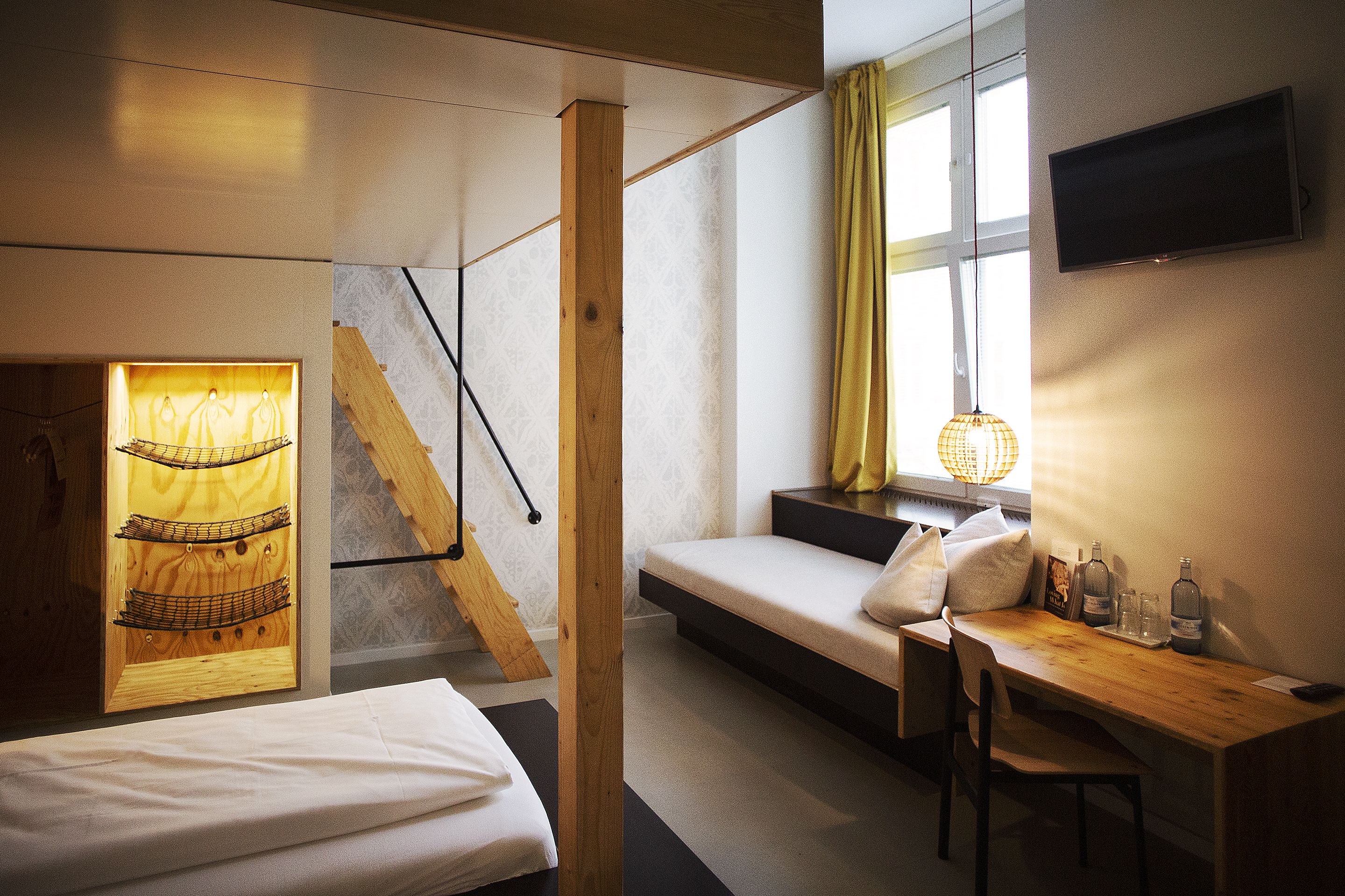 Une chambre moderne avec un lit, un bureau et un canapé. Un téléviseur est fixé au mur et il y a une fenêtre avec des rideaux.