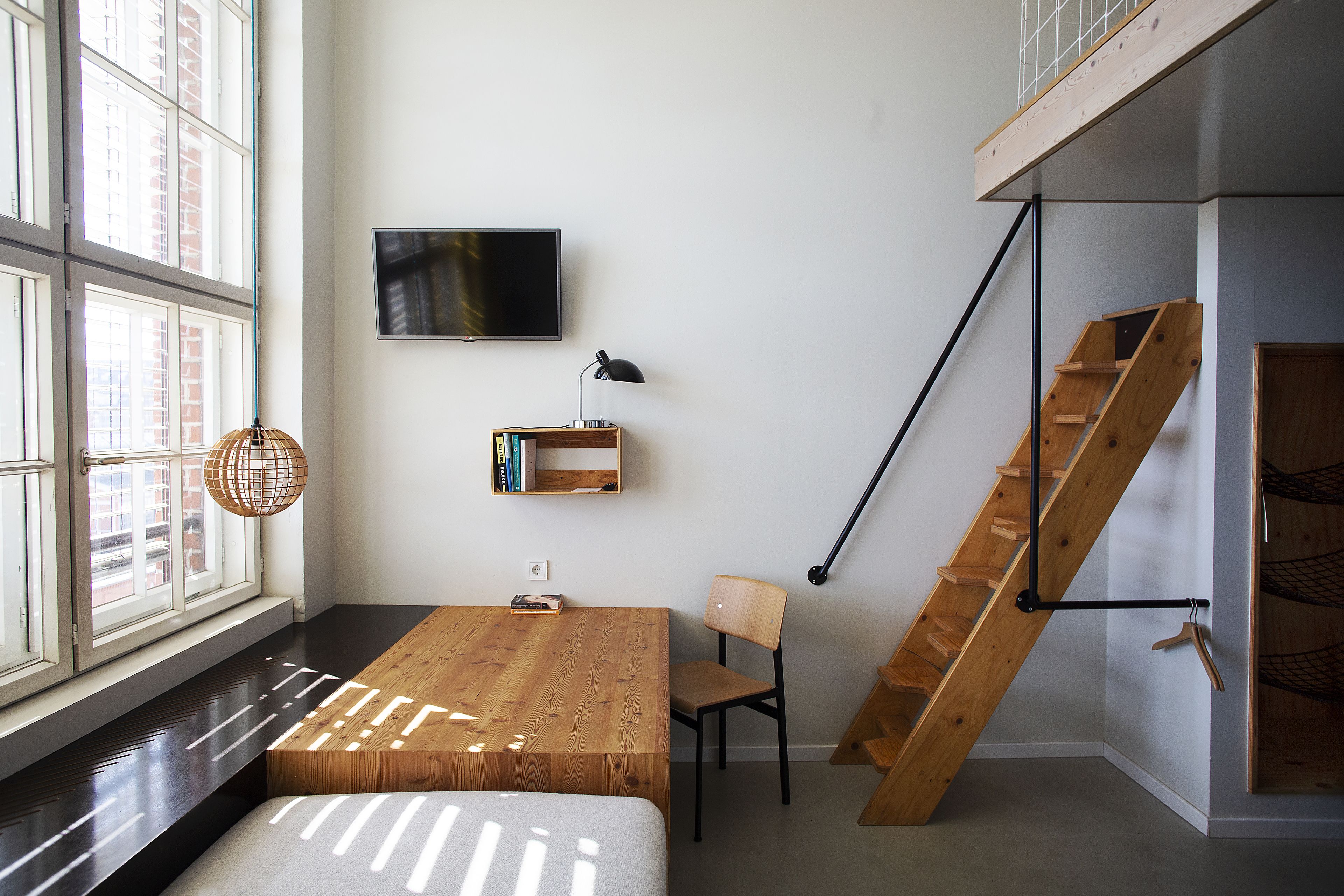 A modern room with a wooden desk, a chair, a TV mounted on the wall, and a wooden staircase.
