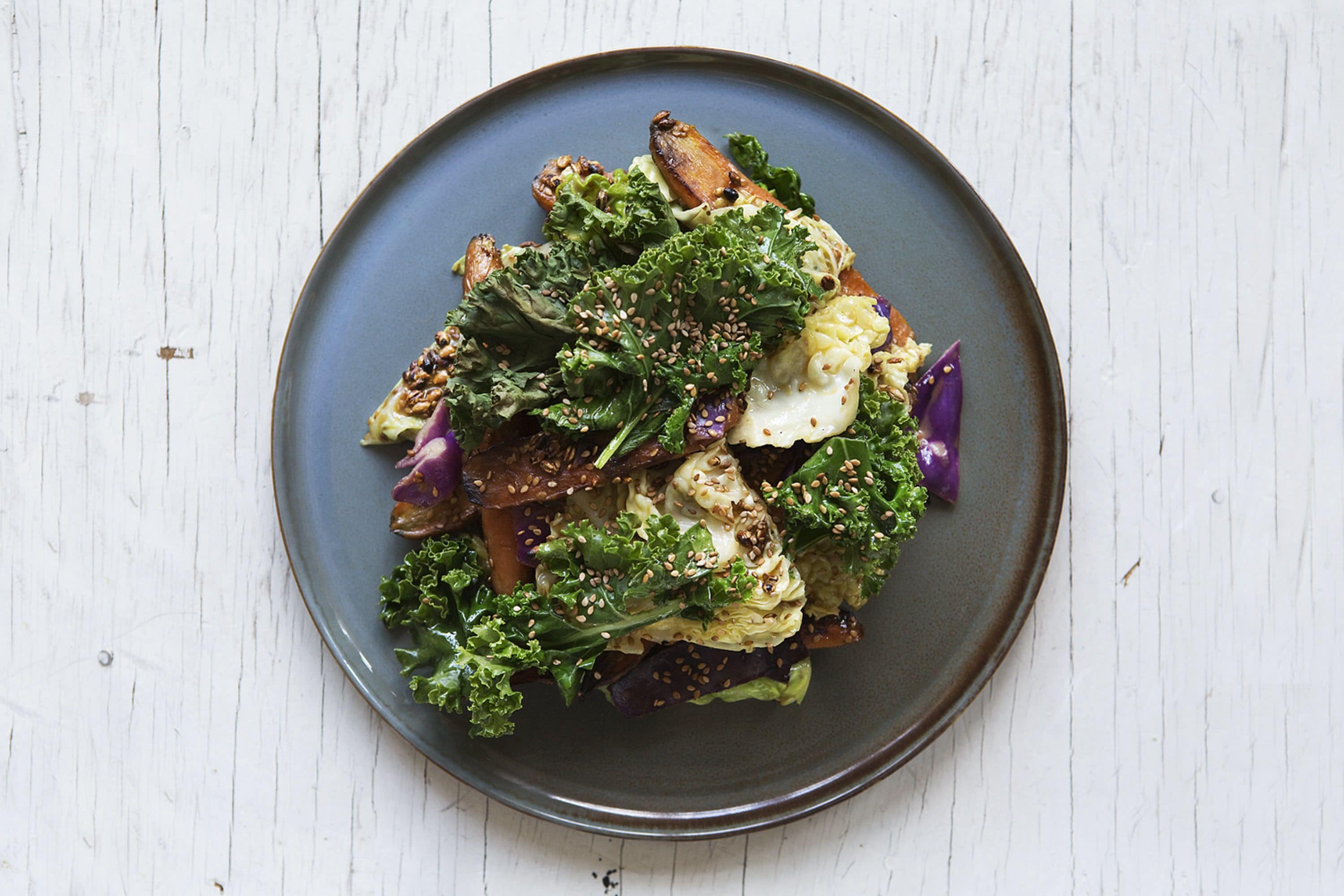 Een bord eten met diverse groenten en een romige topping, geserveerd op een donker bord.