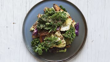 Een bord eten met diverse groenten en een romige topping, geserveerd op een donker bord.