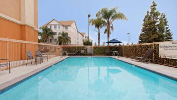 Una piscina al aire libre, sombrillas, sillones reclinables de piscina