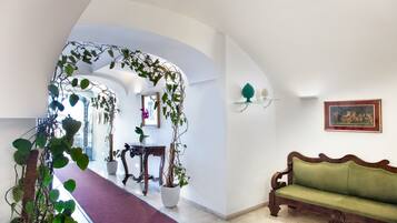 A hallway with a red carpet, a wooden bench, potted plants, and a framed painting on the wall.