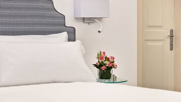 A neatly made bed with white linens, a wall-mounted light fixture, and a small glass vase with flowers on a bedside table.