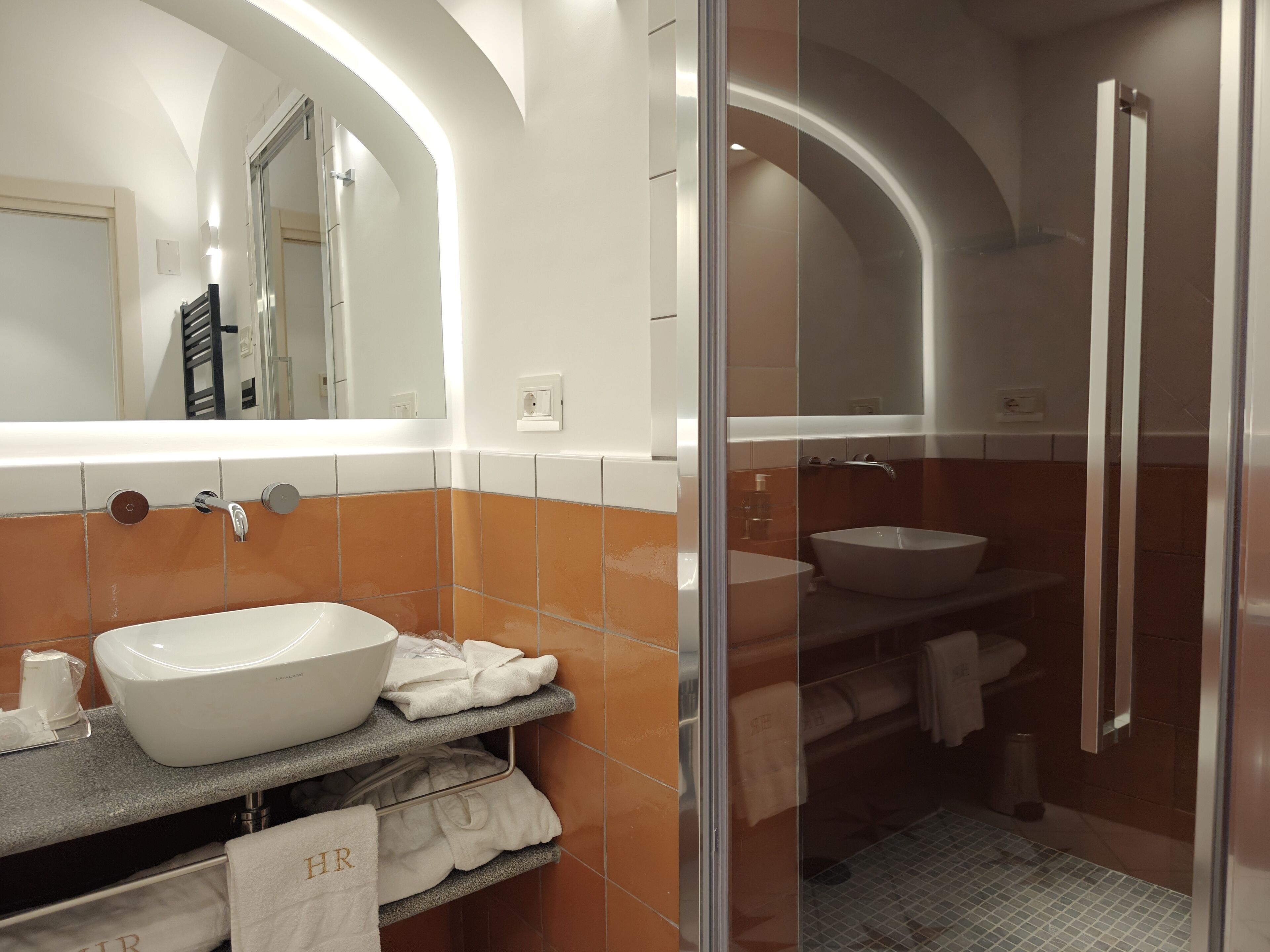 A modern bathroom with a large white sink, a glass-enclosed shower, and a mirror above the sink.
