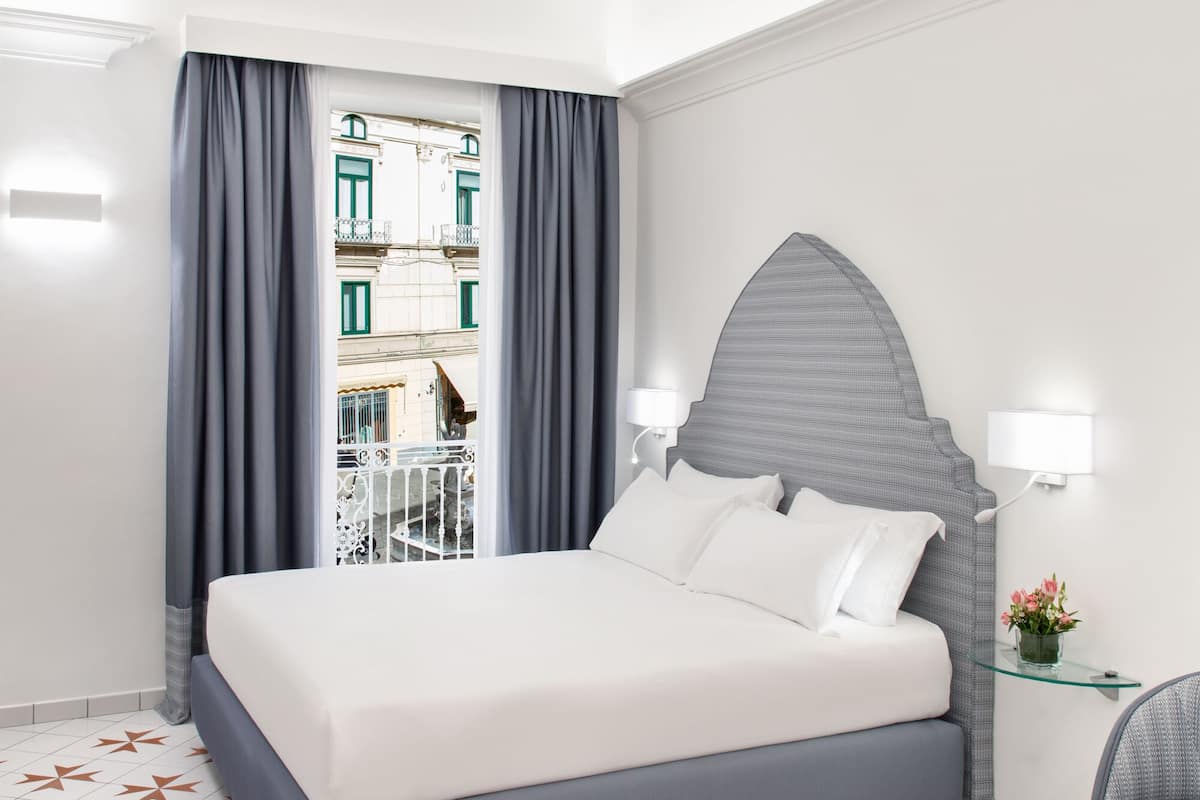 A modern hotel room with a large bed, a view of the city through a window, and a decorative ceiling.
