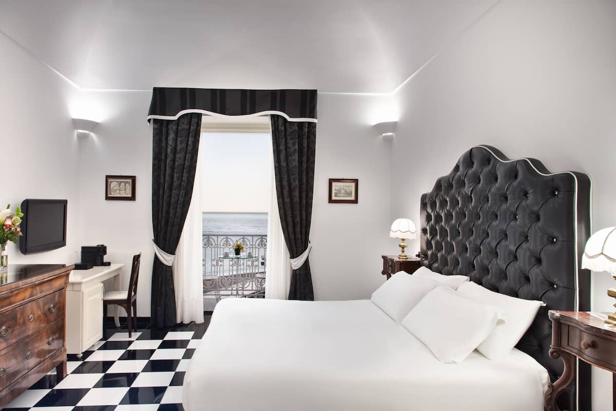A hotel room with a large bed, a desk, a chair, and a view of the sea.