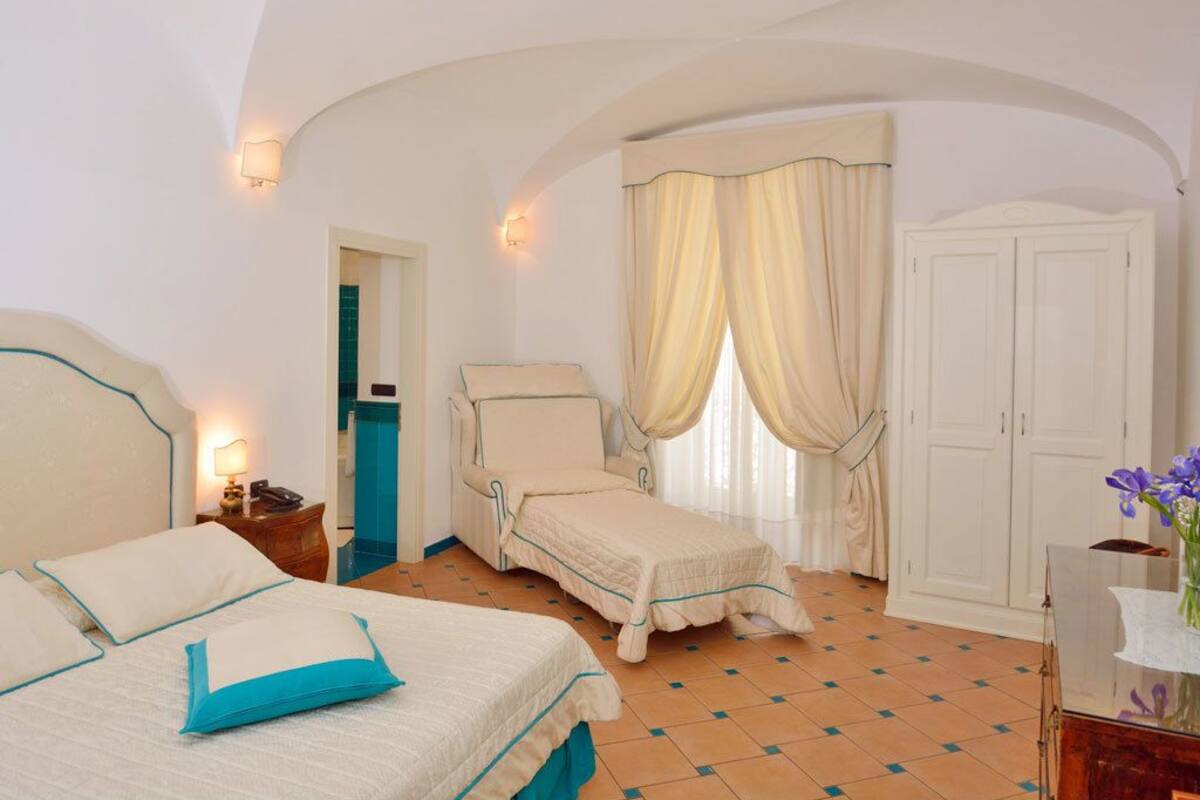 A hotel room with two beds, a sitting area, a wardrobe, and a bathroom visible through an archway.