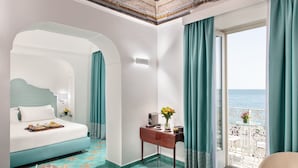 A hotel room with a bed, a desk with a vase of flowers, a view of the sea, and a balcony with chairs. - Hotel Residence - Amalfi (Amalfi)