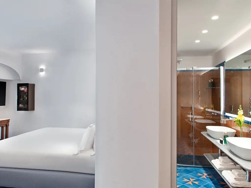 Une chambre d’hôtel moderne équipée d’un lit, d’un grand miroir et d’une salle de bain avec une douche en verre et deux lavabos.