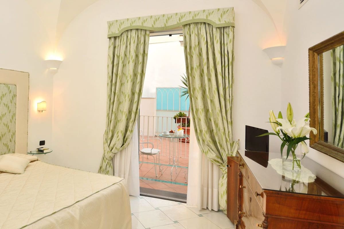 A hotel room with a bed, a bedside table, a mirror, and a view of the outside balcony.