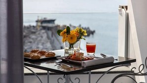 A balcony with a table set for breakfast, including croissants, a sandwich, and a glass of juice, with a view of the sea and a rocky shoreline. - Hotel Residence - Amalfi (Amalfi)