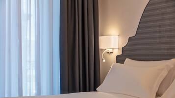 Habitación de hotel con cama, cortinas, lámpara de pared y ventana con cortinas translúcidas.