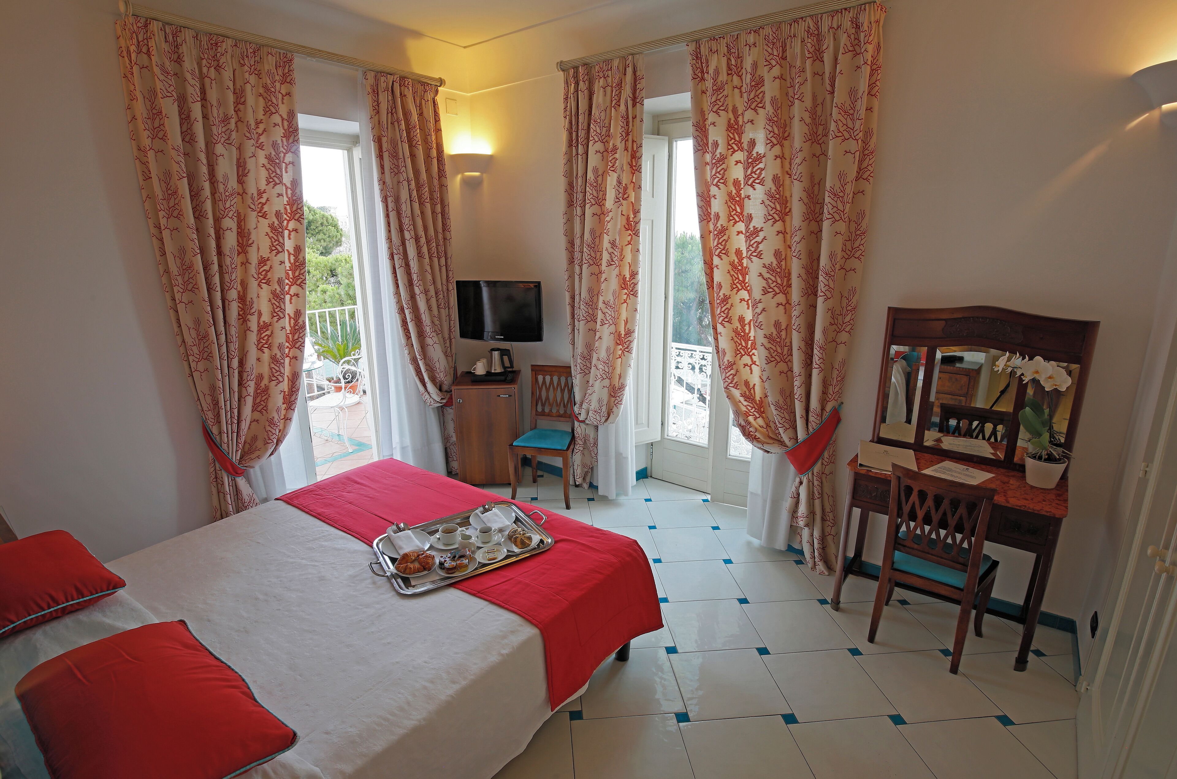 Une chambre d’hôtel avec un lit, un bureau, une chaise, une télévision et un balcon avec des rideaux.