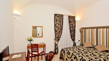 A hotel room with a bed, a desk, a chair, a small table, a mirror, and curtains.