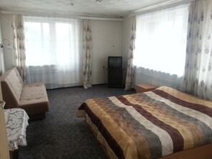 A hotel room with a bed, a sofa, a television, and curtains. - Jeruzale Hotel (Vilnius)