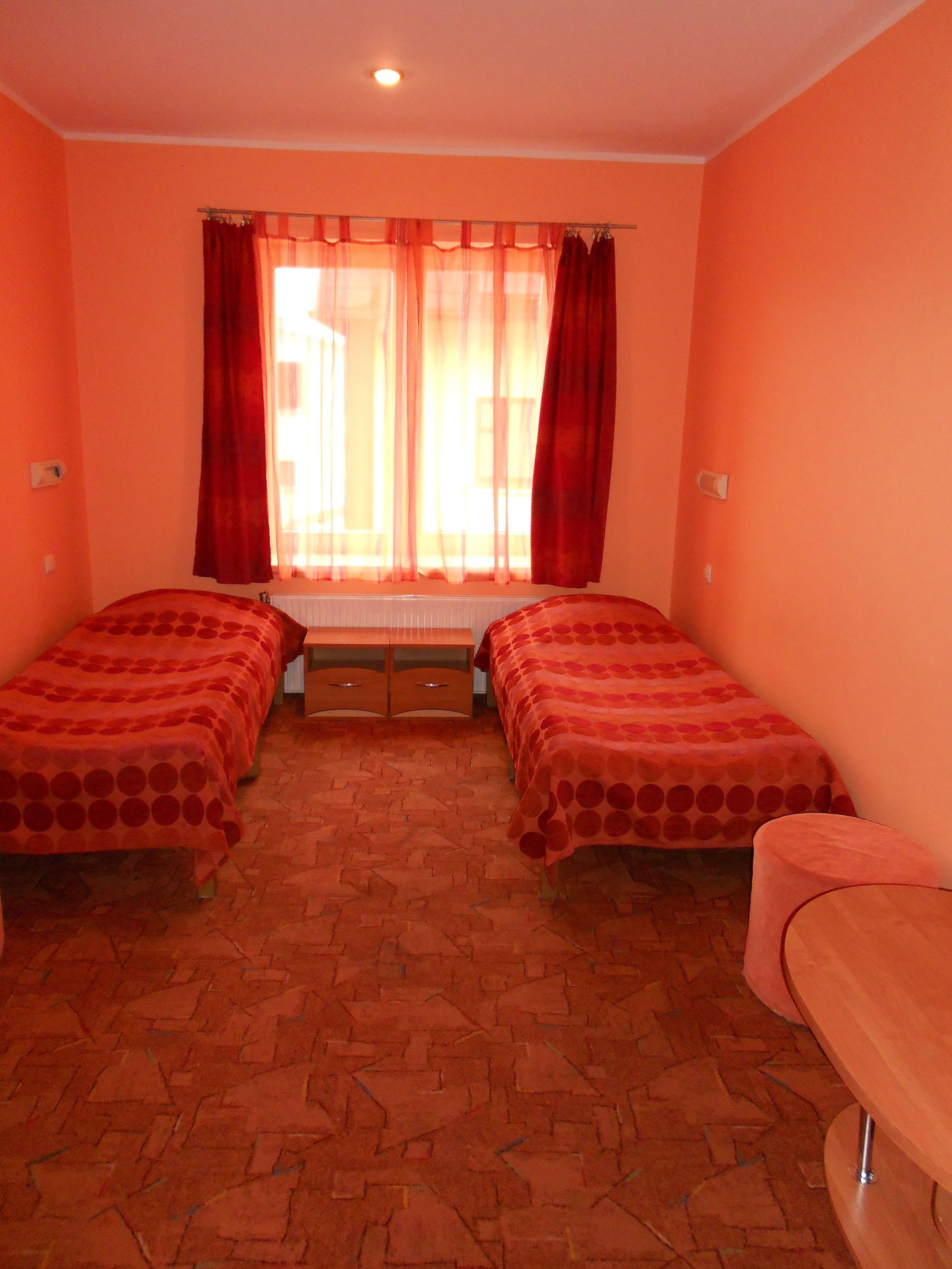 A room with two beds, a window with curtains, a radiator, and a bench.