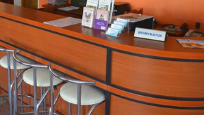 A reception area with a wooden counter, bar stools, a television mounted on the wall, and a shelf with various items including books and a flag. - Jeruzale Hotel (Vilnius)