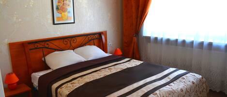 A neatly made bed with a patterned bedspread, a wooden headboard, and a framed picture on the wall.