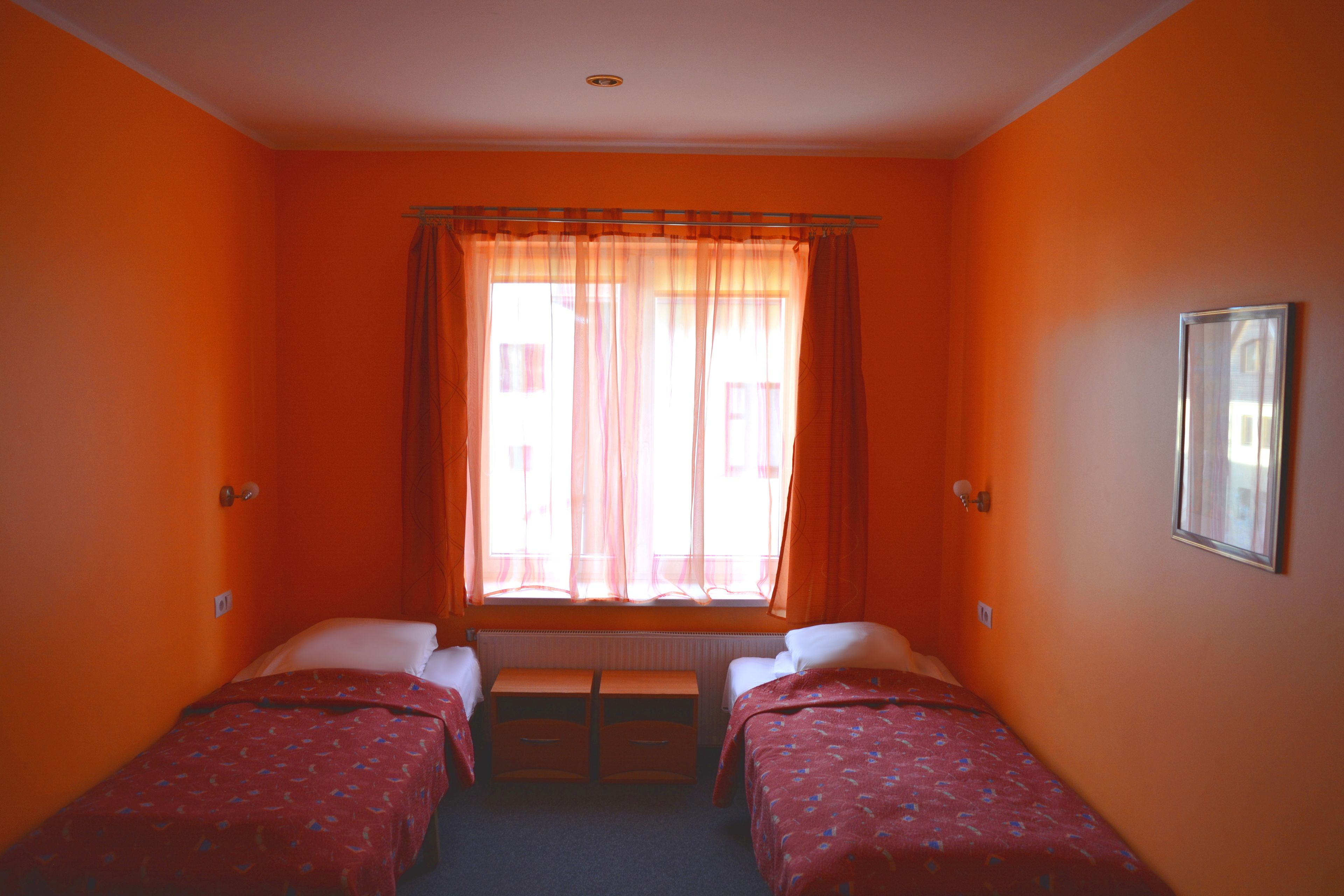 A room with two single beds, a window with sheer curtains, and a radiator.