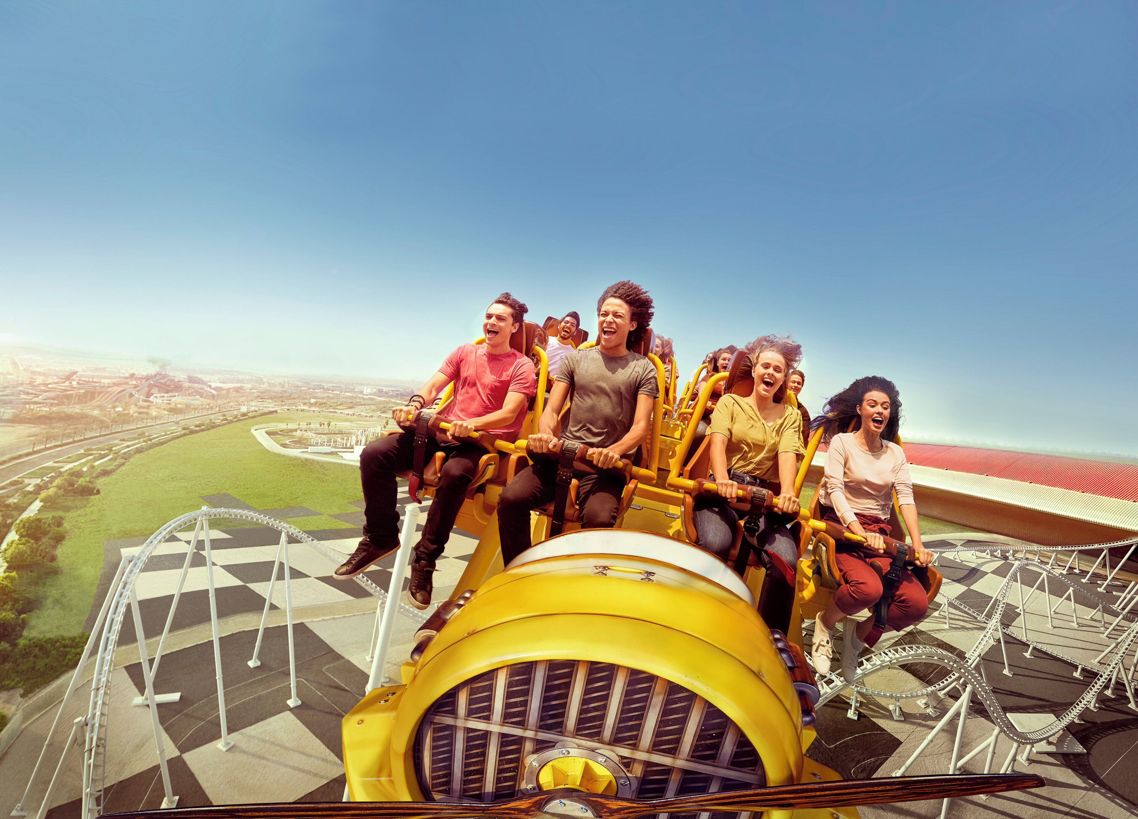 A group of people on a yellow amusement ride with a view of a stadium and cityscape.
