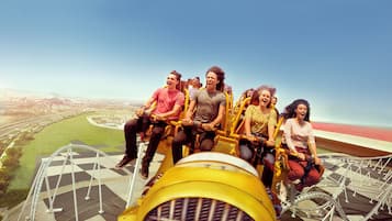 A group of people on a yellow amusement ride with a view of a stadium and cityscape.