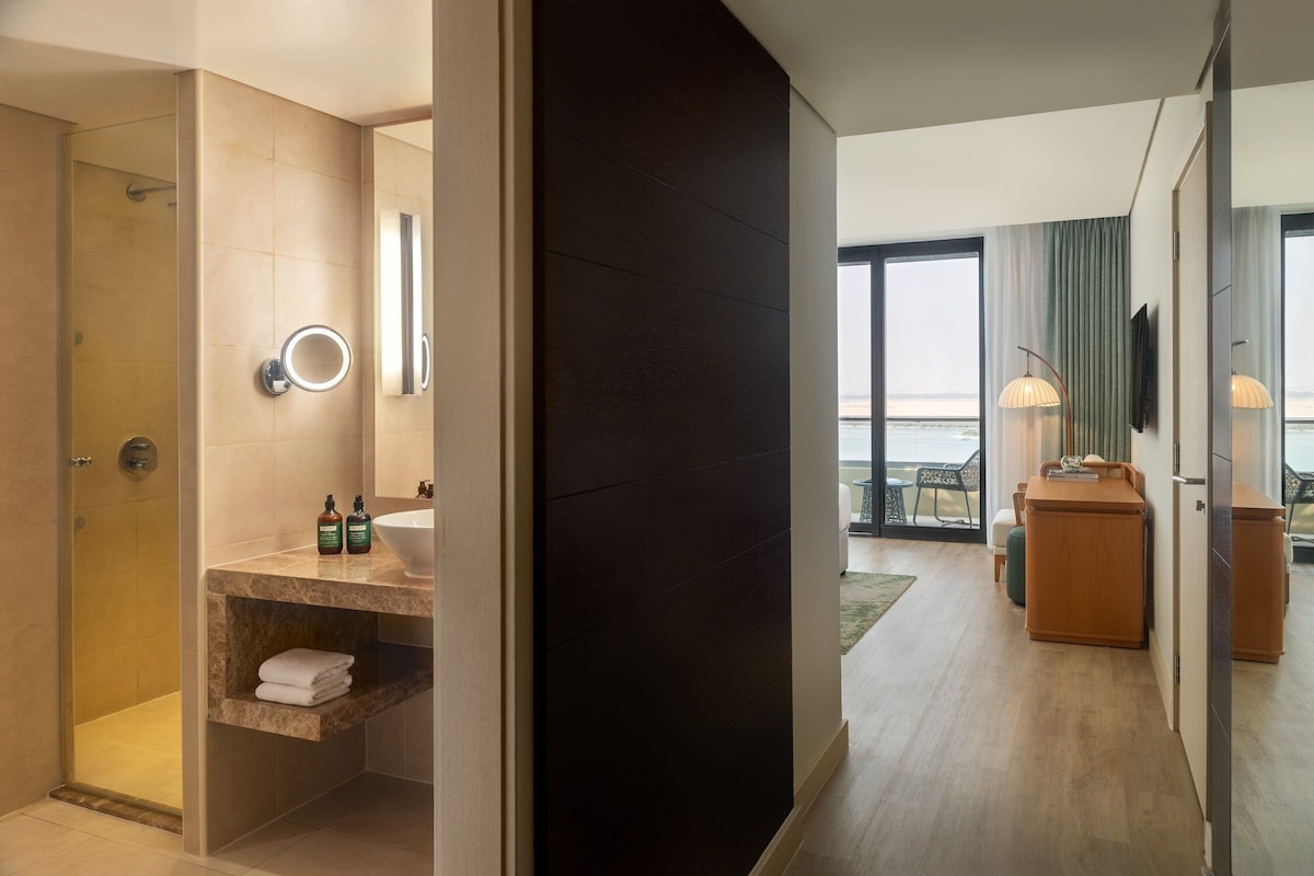 Un baño de hotel moderno con ducha, tocador y vista al mar.