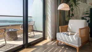 A balcony with wicker chairs, a white sofa, and a large window offering a view of the sea.