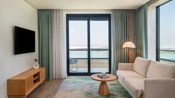 Ein Hotelzimmer mit großem Fenster, einer Couch, einem an der Wand montierten Fernseher, einem kleinen Holztisch und einer Lampe.